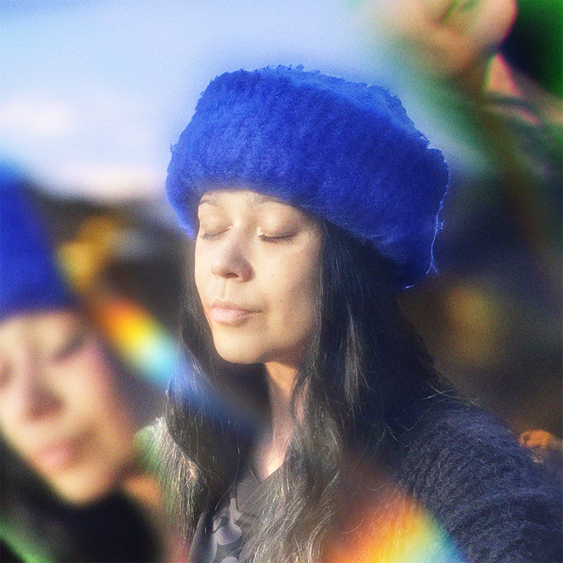 Person wearing a blue hand-knitted mohair beanie with eyes closed, surrounded by a prism effect.