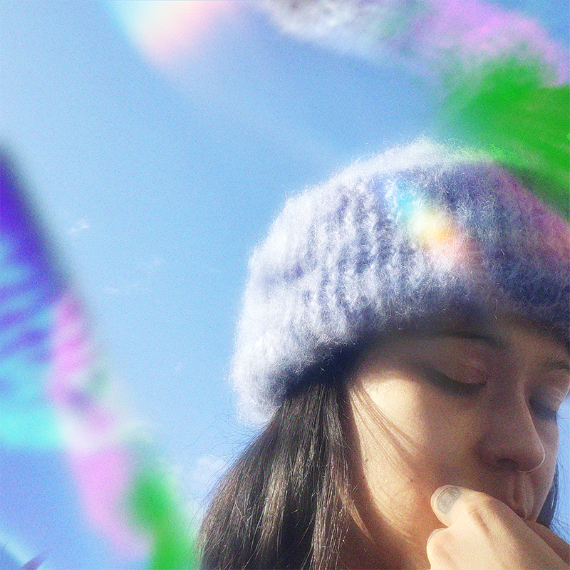 Person wearing a light blue hand-knitted mohair beanie with eyes closed, surrounded by a prism effect.