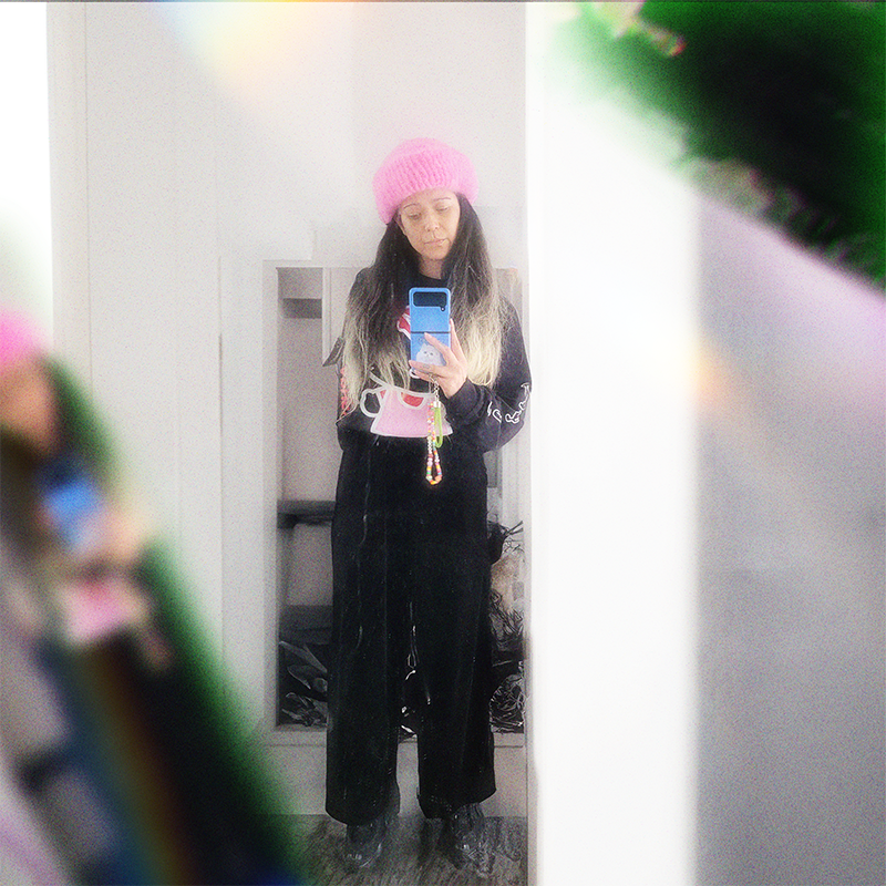 Person wearing a pink hand-knitted mohair beanie taking a selfie in a mirror, surrounded by a prism effect.